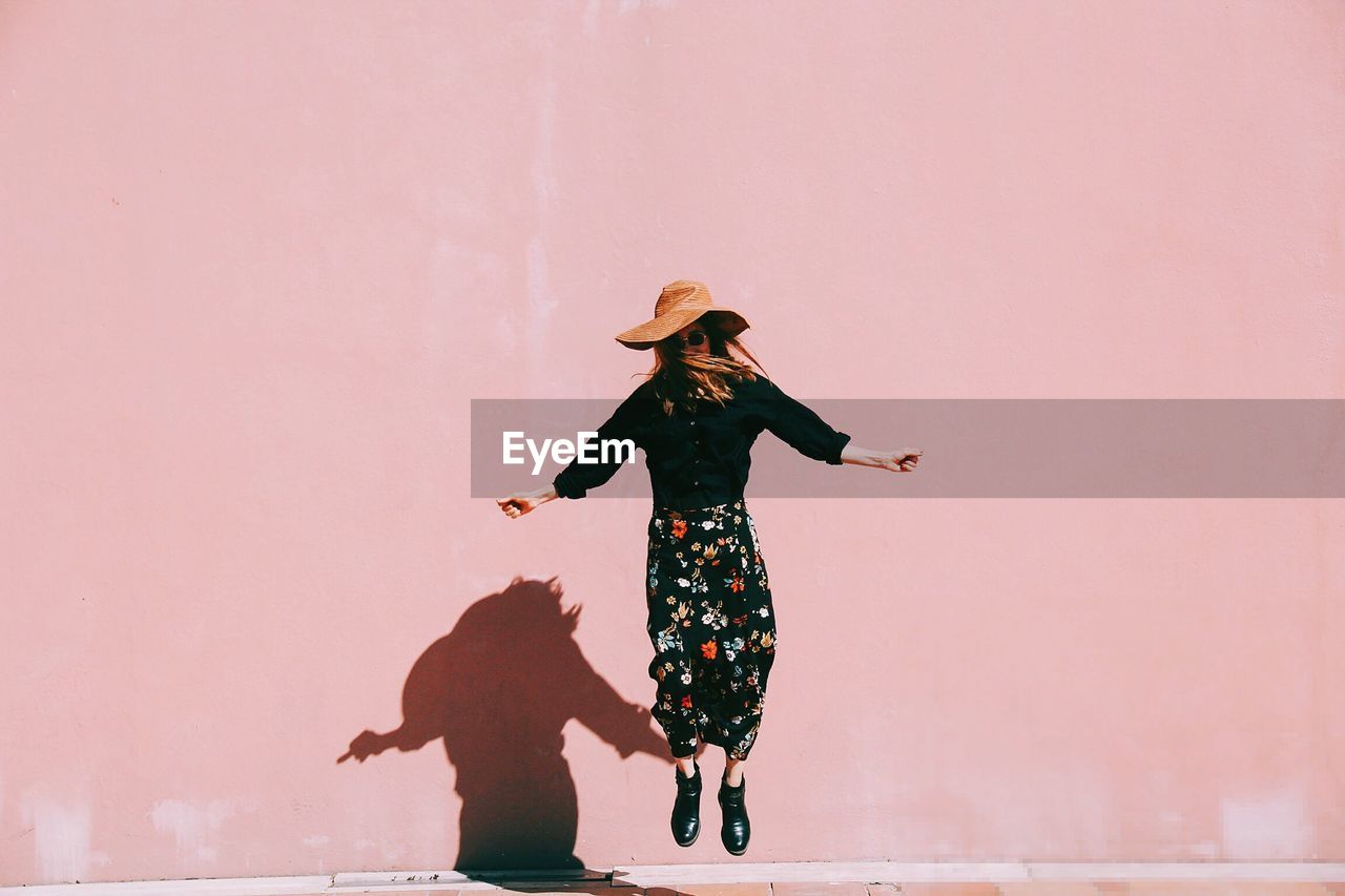 Woman jumping against pink wall