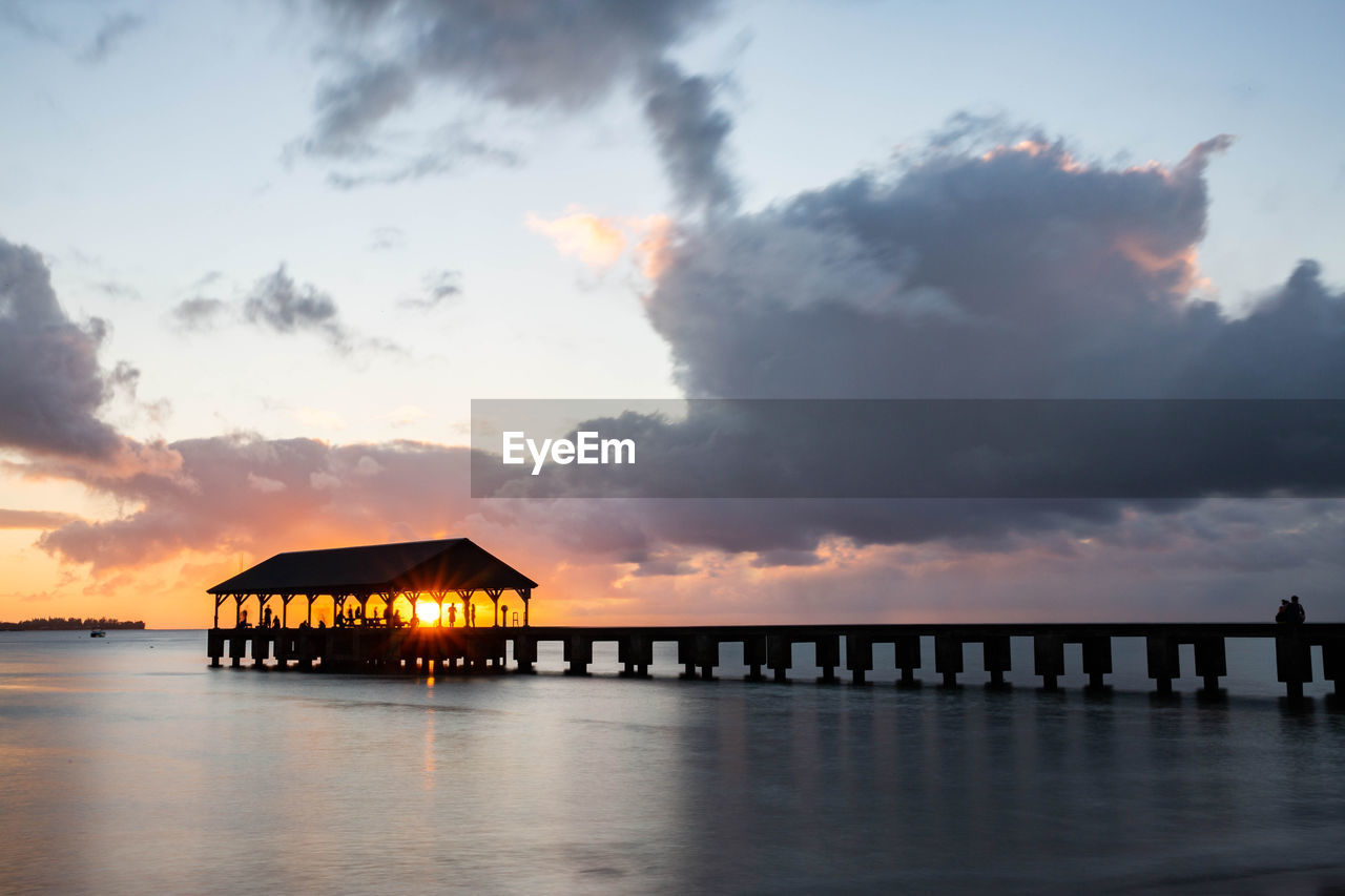 SILHOUETTE WOODEN POST IN SEA AGAINST SKY DURING SUNSET