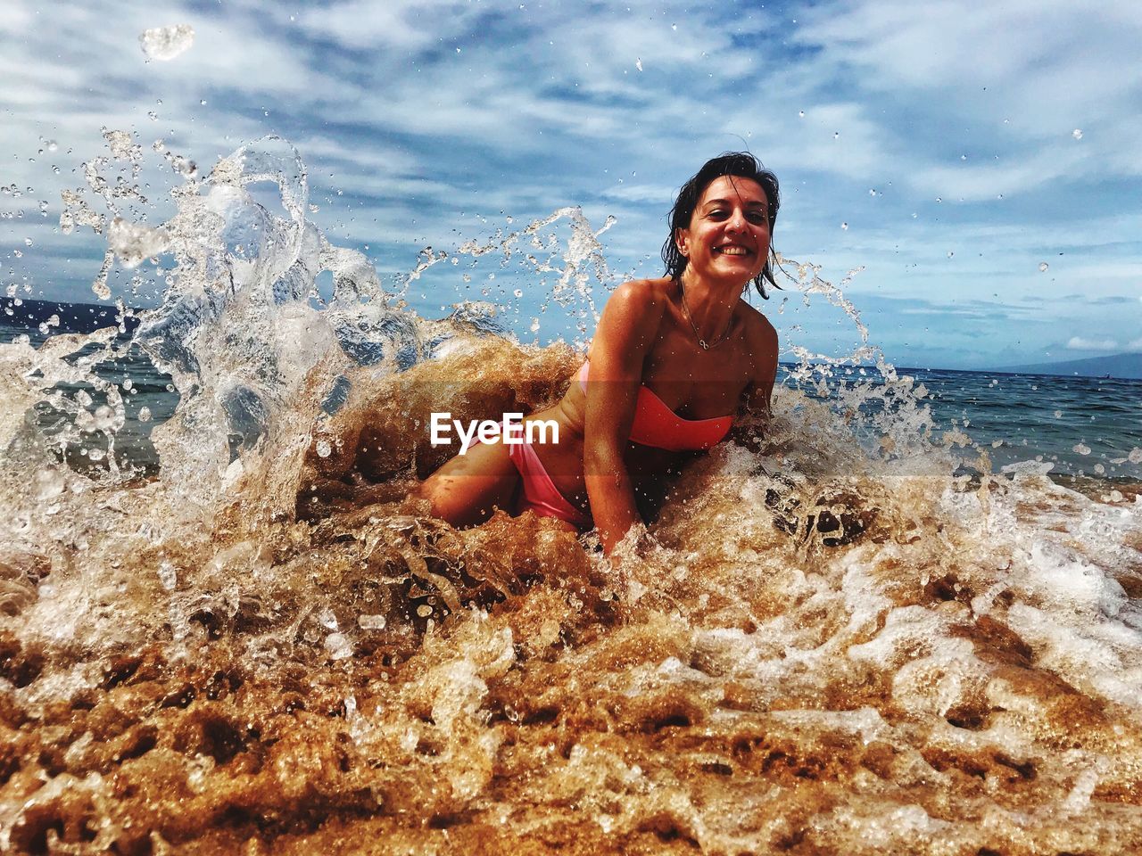 Portrait of smiling woman playing in waves on shore at beach