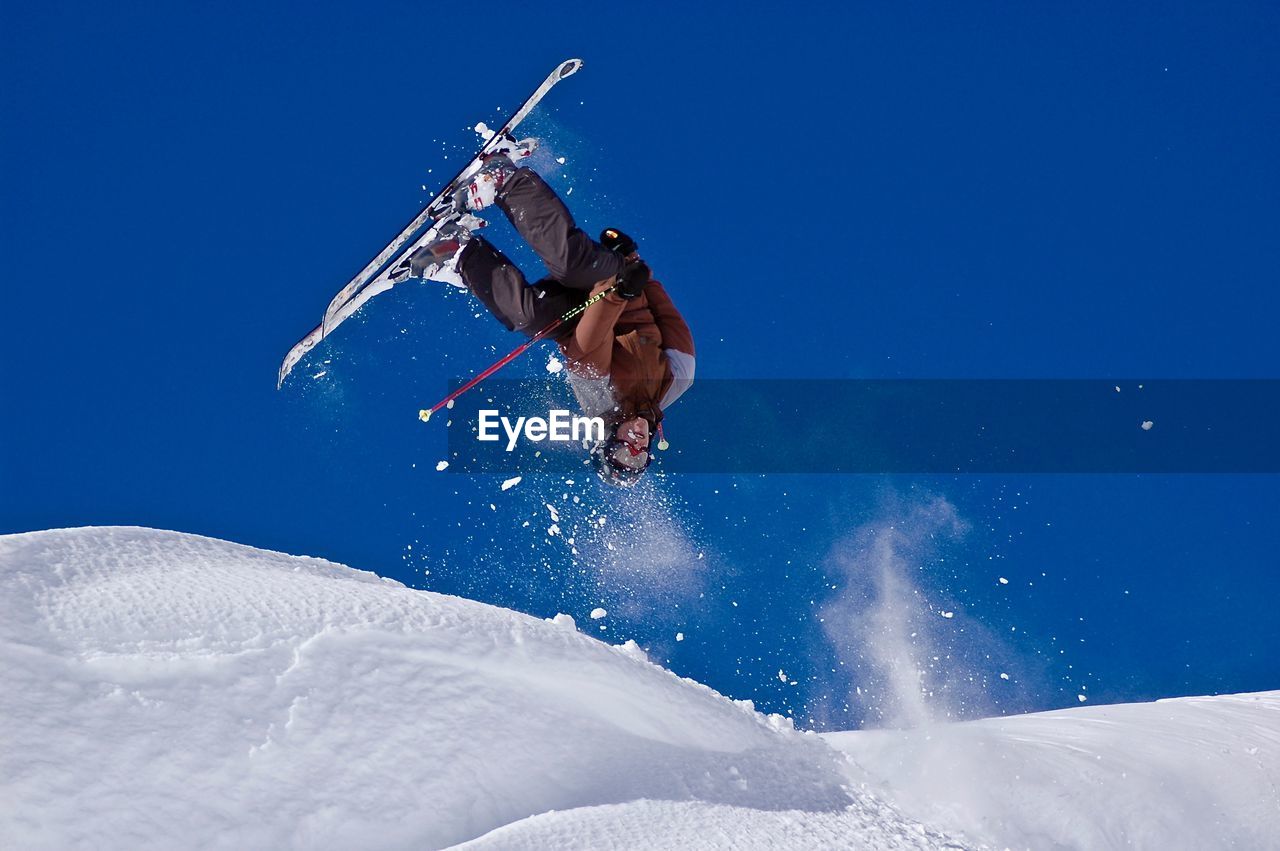 Low angle view of man jumping on snowcapped mountain against sky