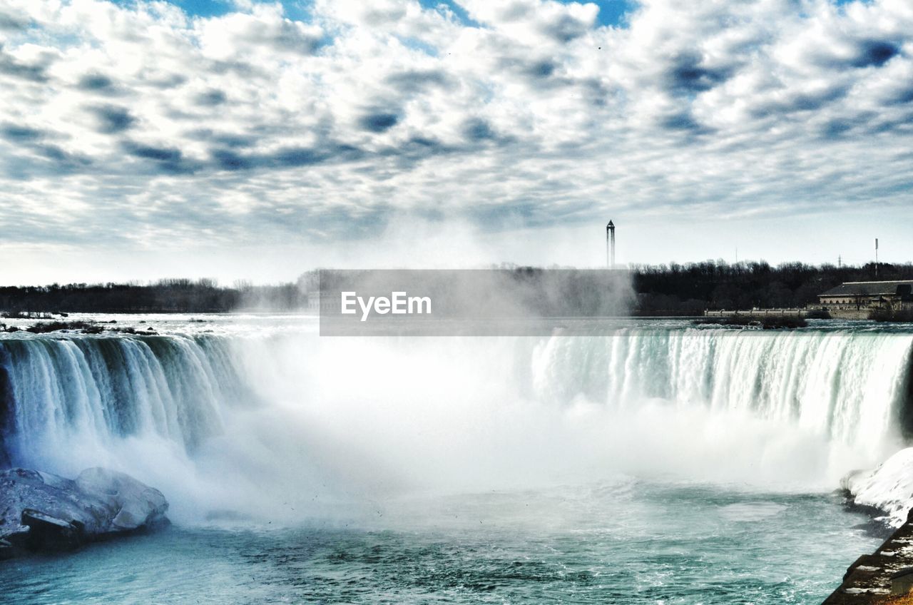 Scenic view of waterfall against cloudy sky