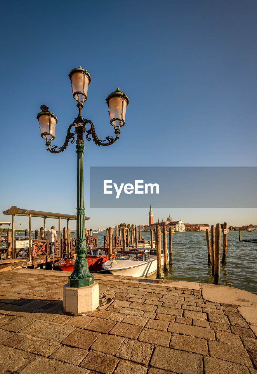 Street light on pier by grand canal against clear blue sky