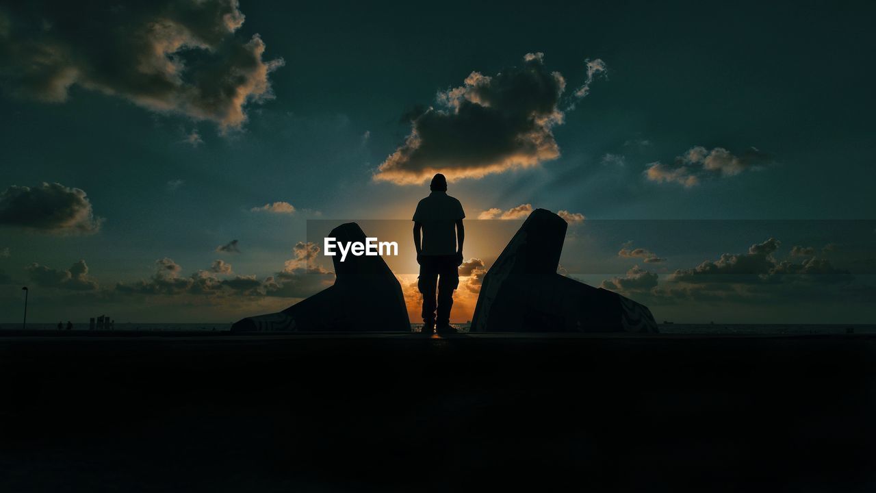 Rear view silhouette of man standing by sea against sky during sunset