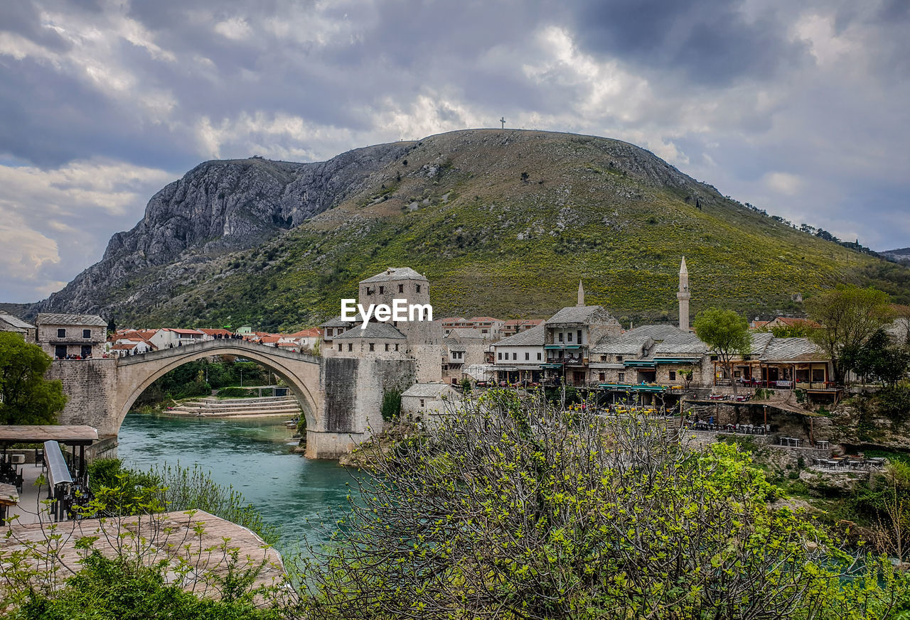 BRIDGE OVER RIVER AMIDST BUILDINGS AGAINST SKY