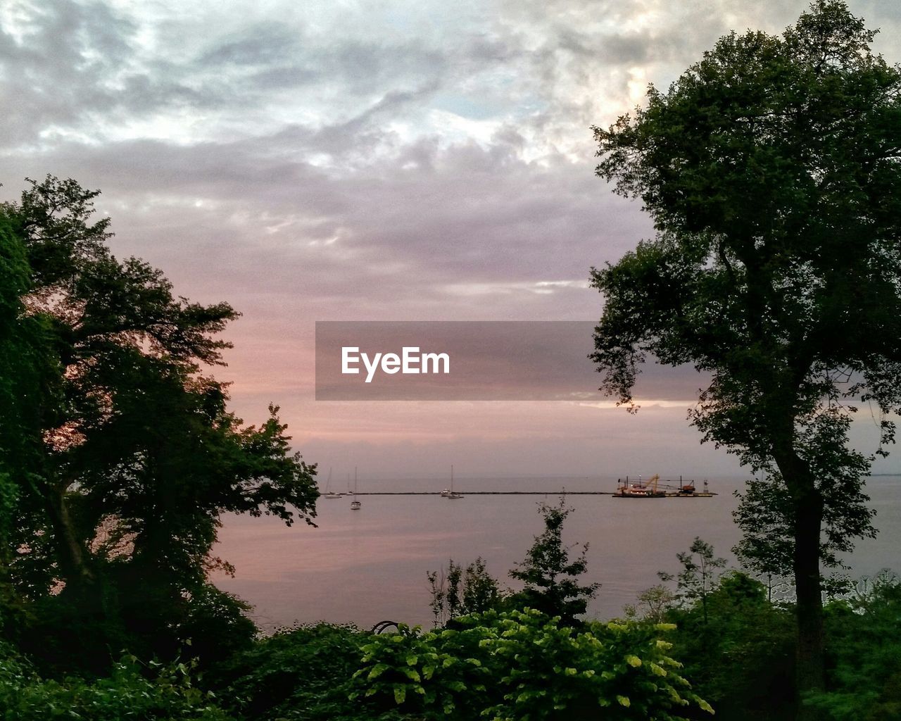 Idyllic shot of sailboats by jetty against cloudy sunset sky