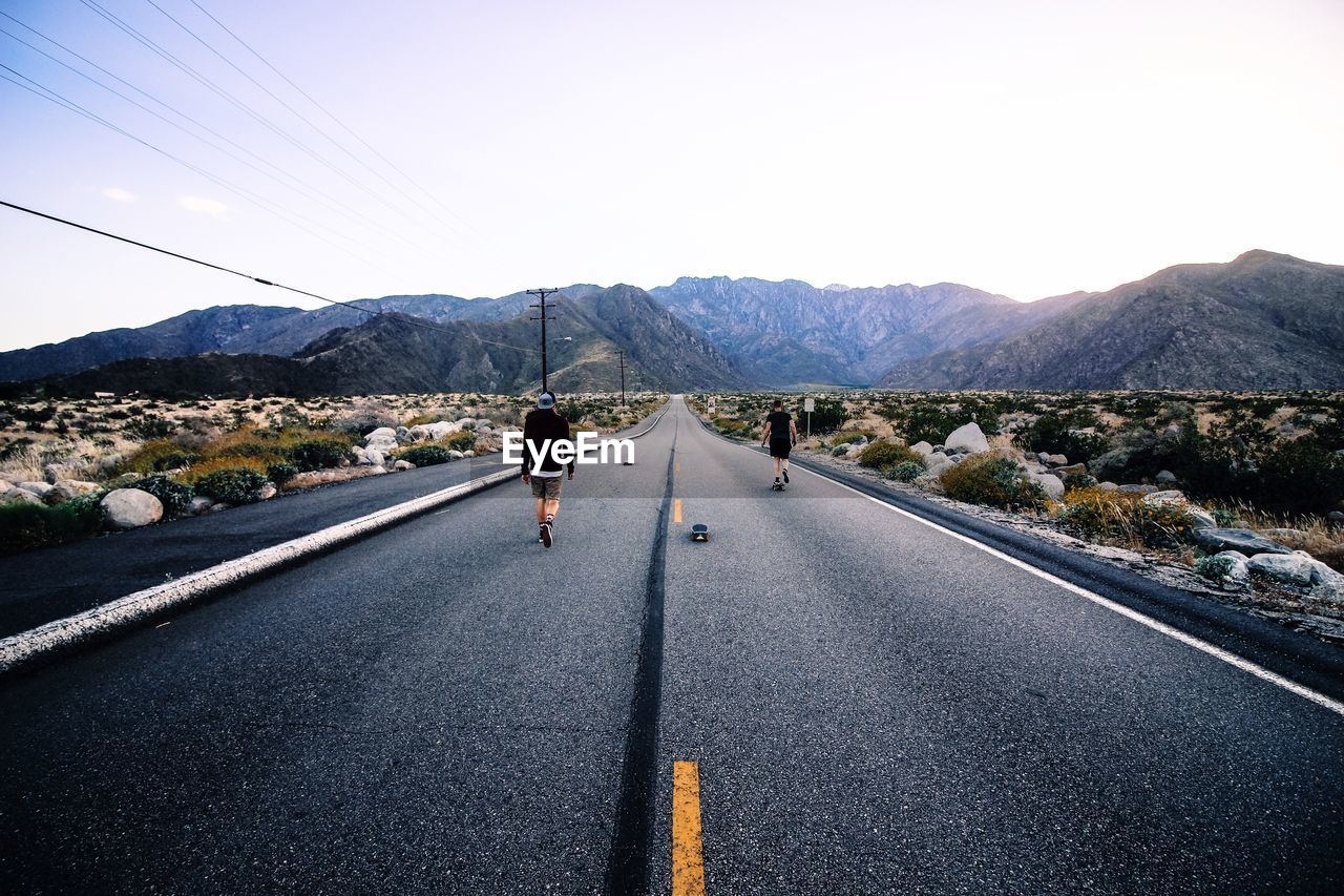 Rear view of men walking on road against mountain range