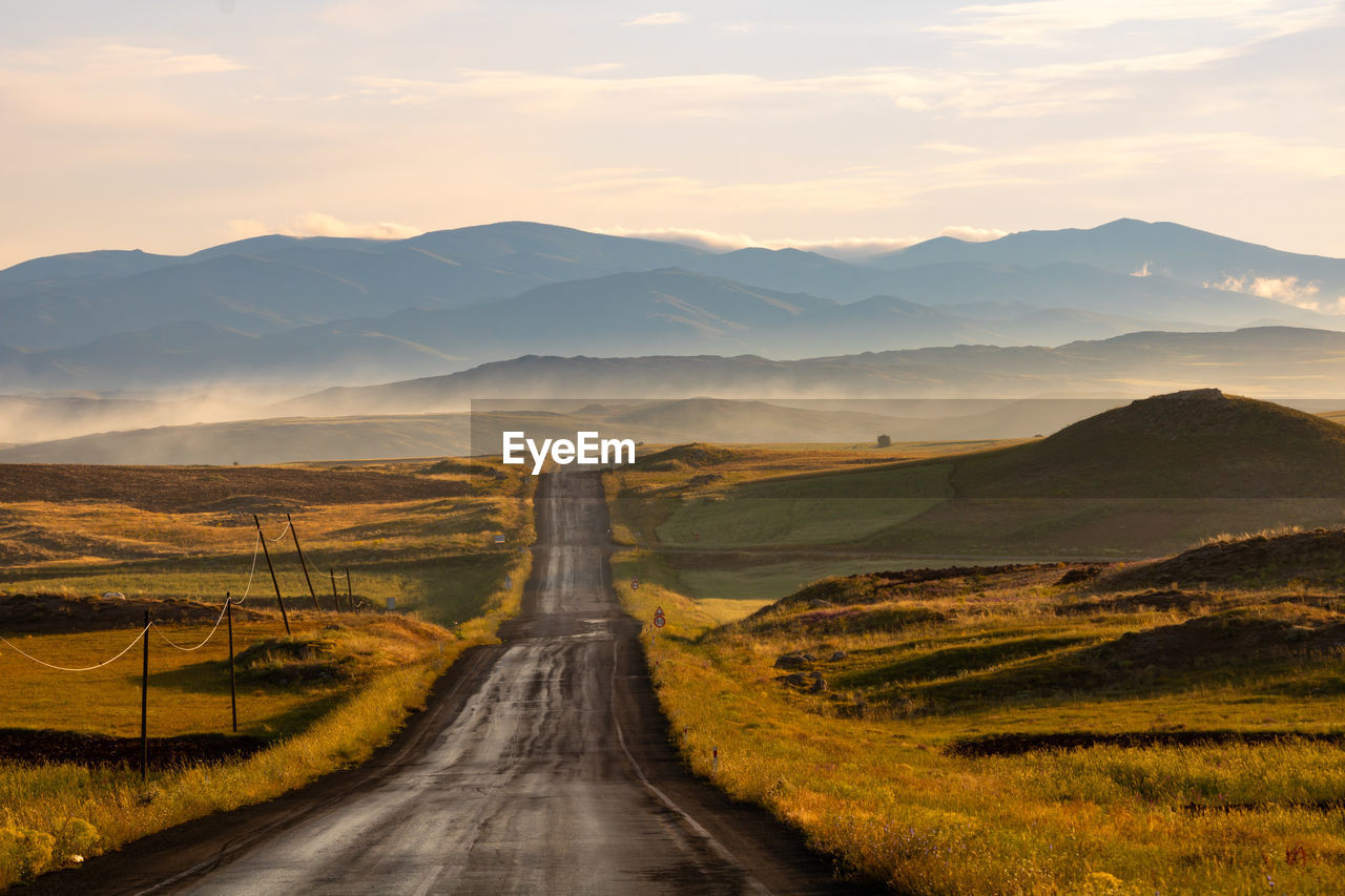 Countryroad at sunrise with hills and fog on the background