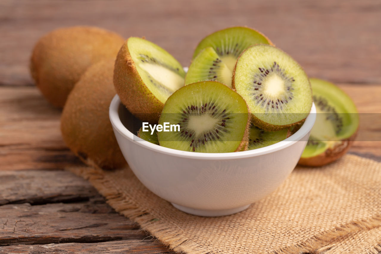 Fresh kiwi slice in the white bowl on the brown sack on the old wooden table