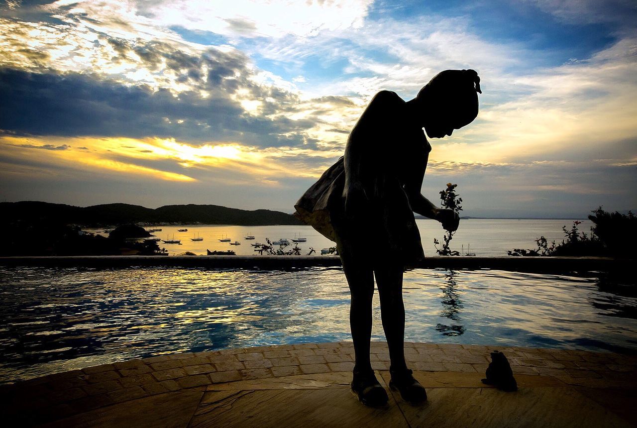 Silhouette girl standing by swimming pool against sky during sunset