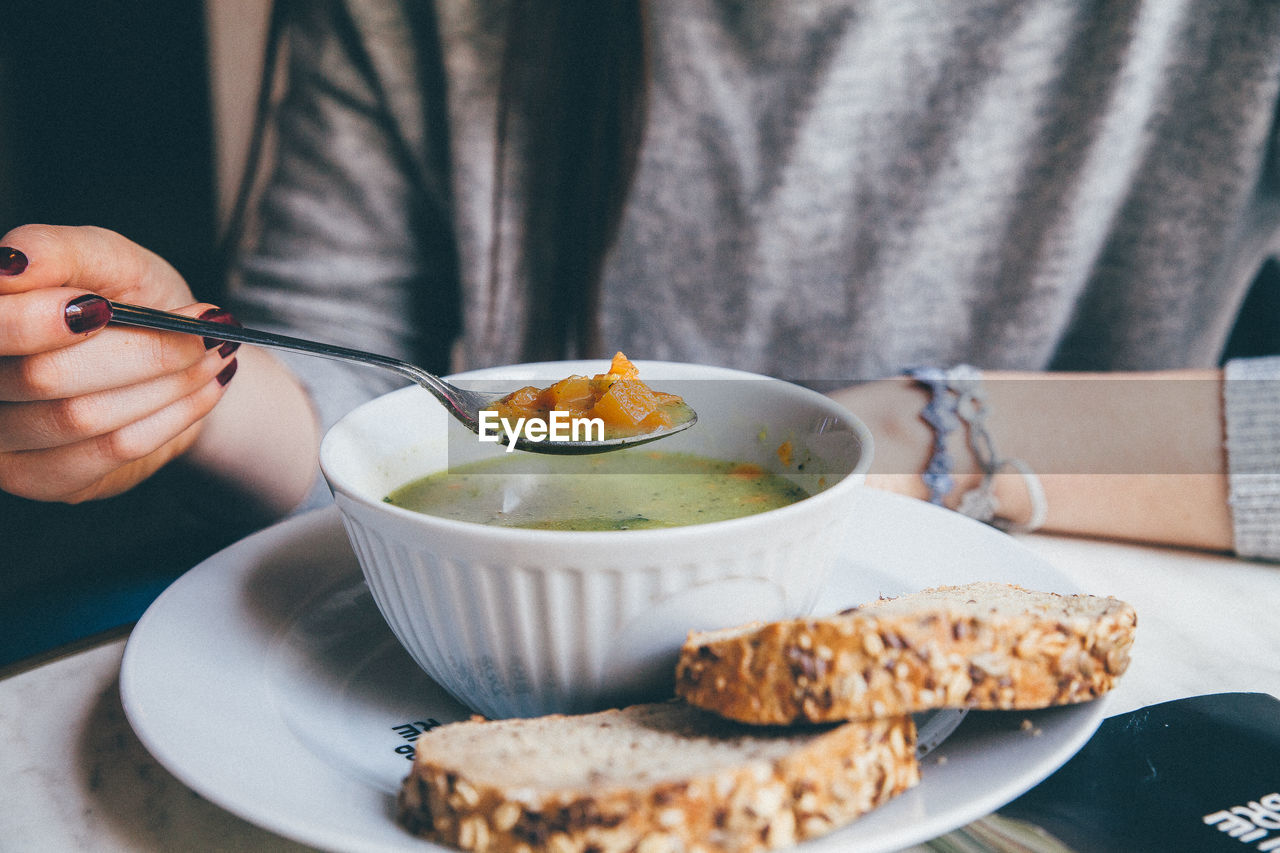 Midsection of woman holding spoon over soup