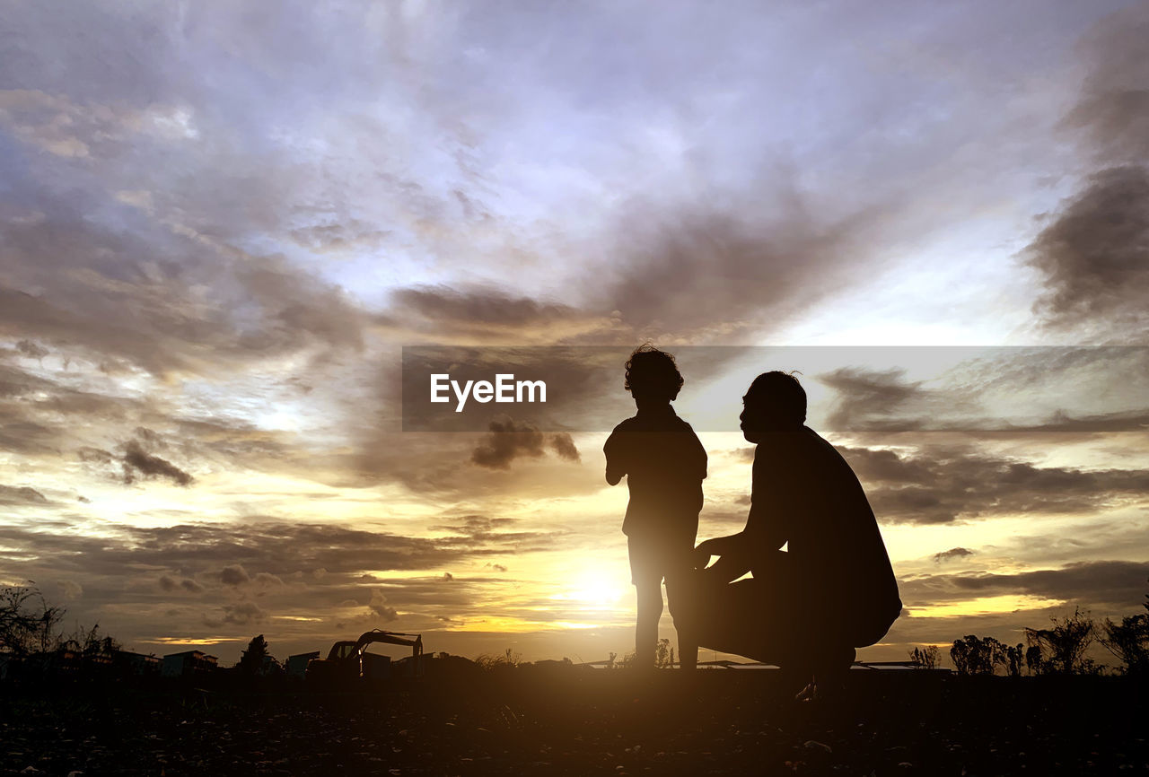 Silhouette father and son on land against sky during sunset