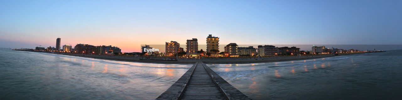 Beach promenade in italy, panoramic view of buildings against sky during sunset