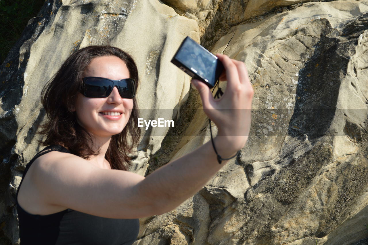 Happy woman taking selfie from camera against rock formation