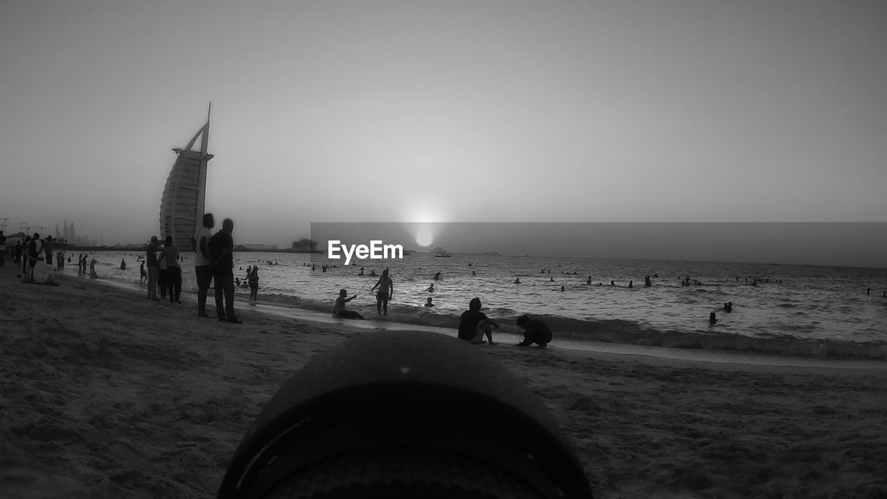 People on sandy beach against burj al arab