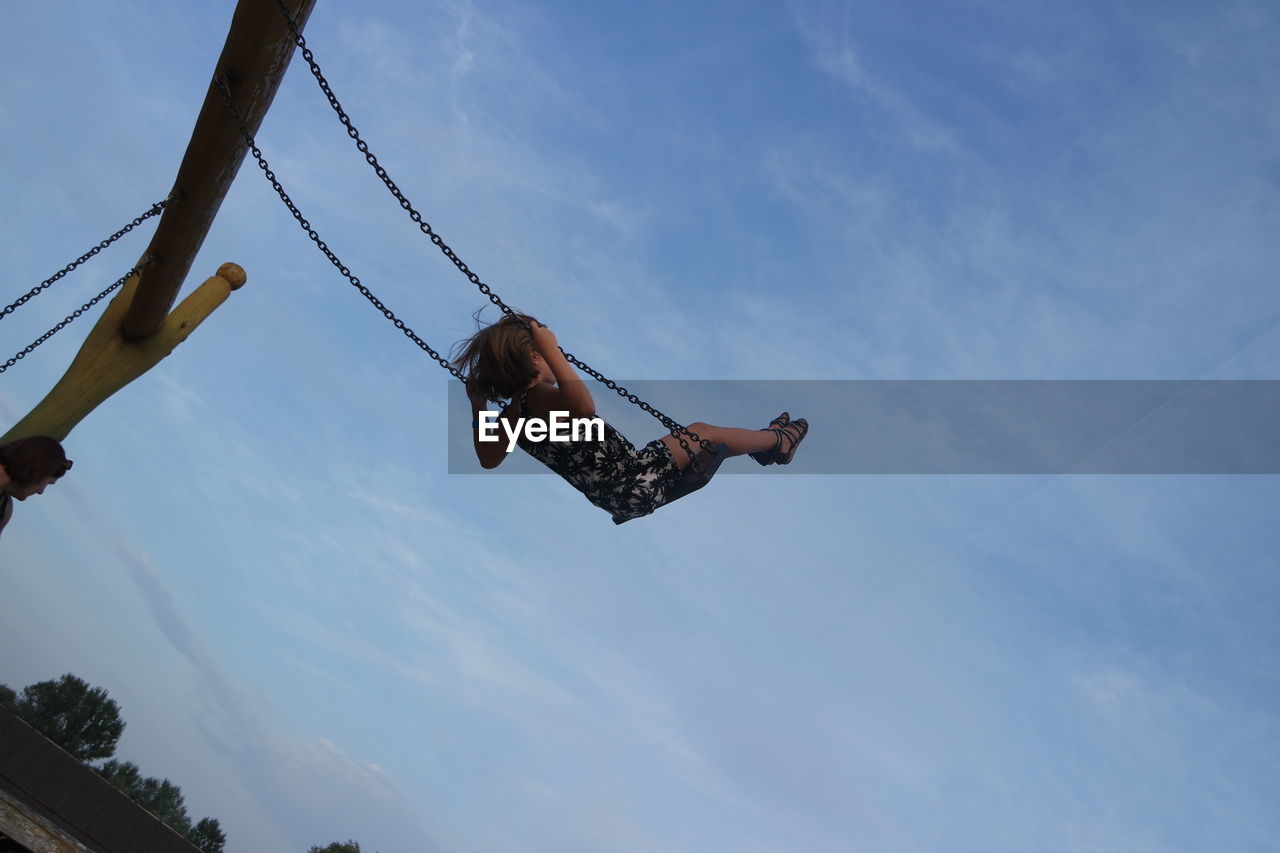 Low angle view of girl in swing against sky