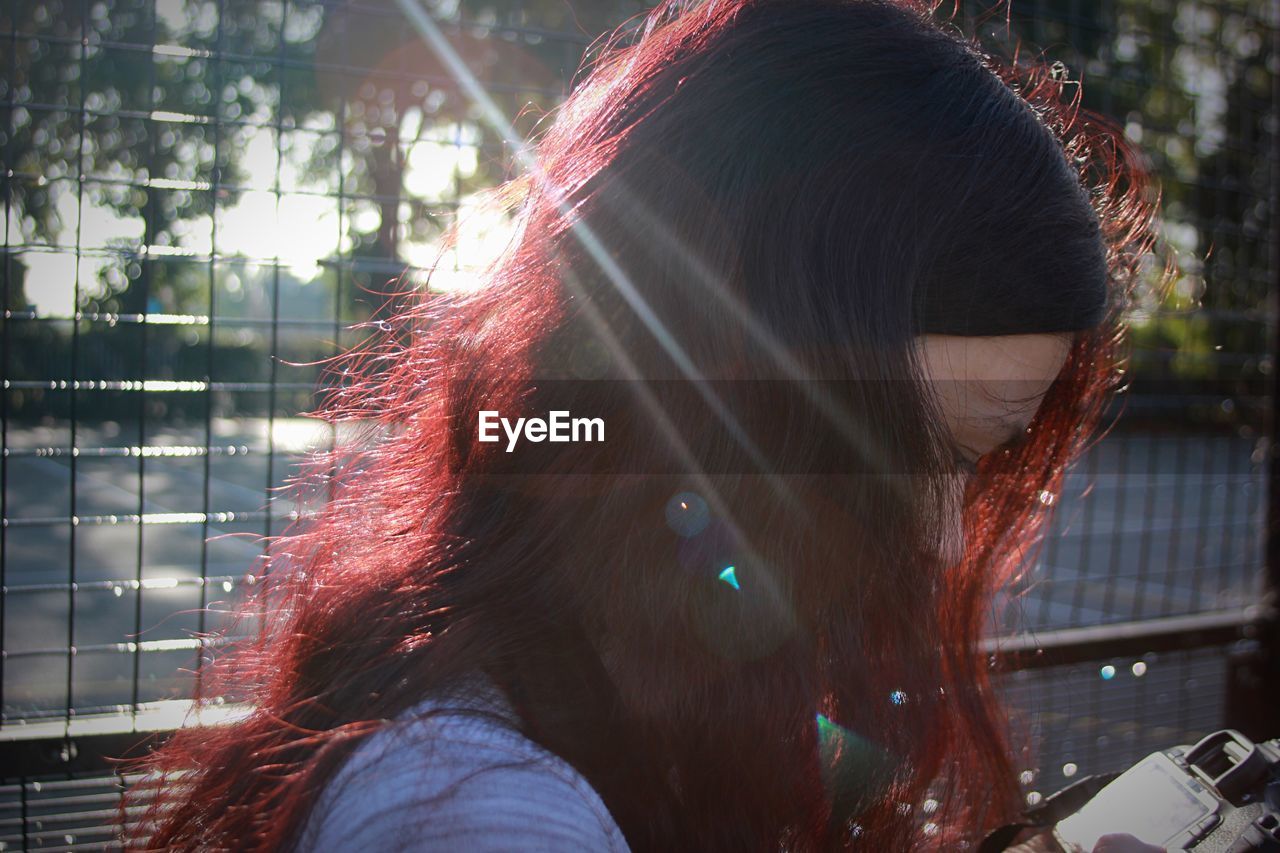 Close-up of sunlight falling on young woman by fence