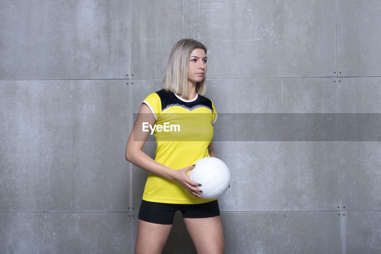 Woman holding sports ball while standing against wall