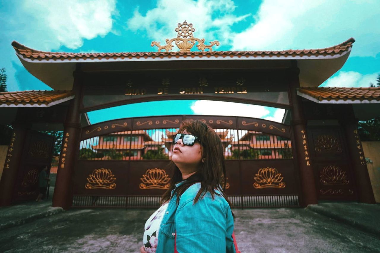 PORTRAIT OF YOUNG WOMAN STANDING AGAINST BUILT STRUCTURE