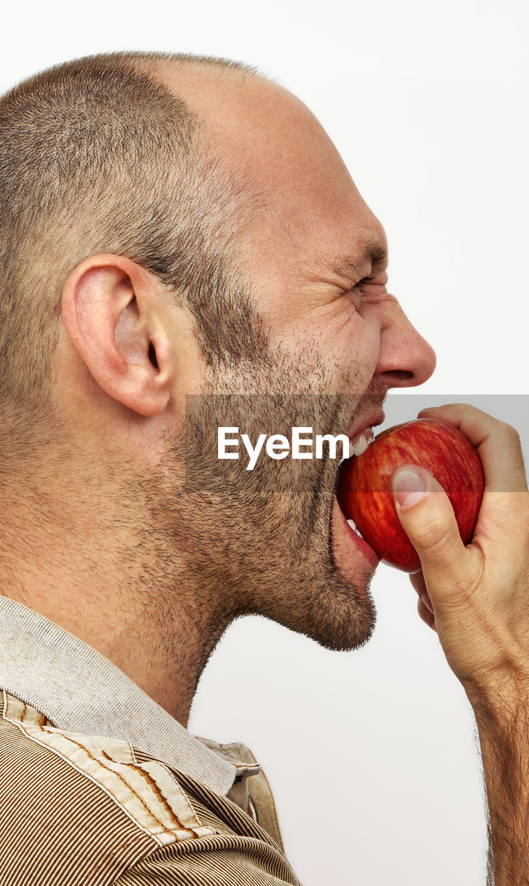 Close-up of man eating apple against white background