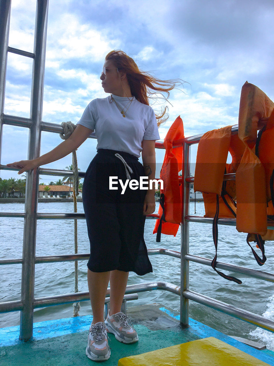 YOUNG WOMAN STANDING BY RAILING AGAINST SKY