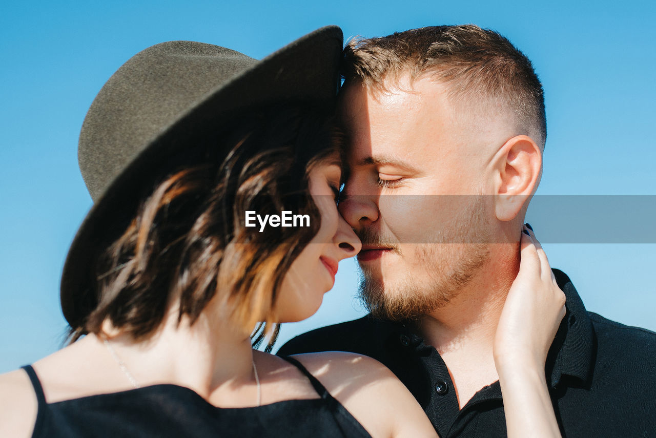 PORTRAIT OF MAN AND WOMAN WEARING HAT AGAINST BLUE SKY