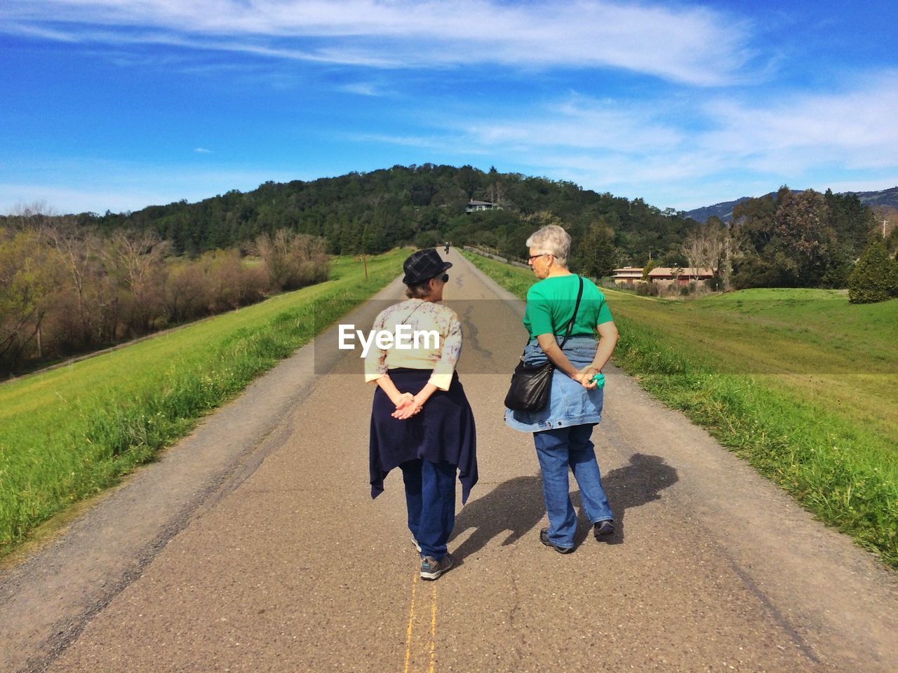 REAR VIEW OF MAN WALKING ON ROAD IN FIELD