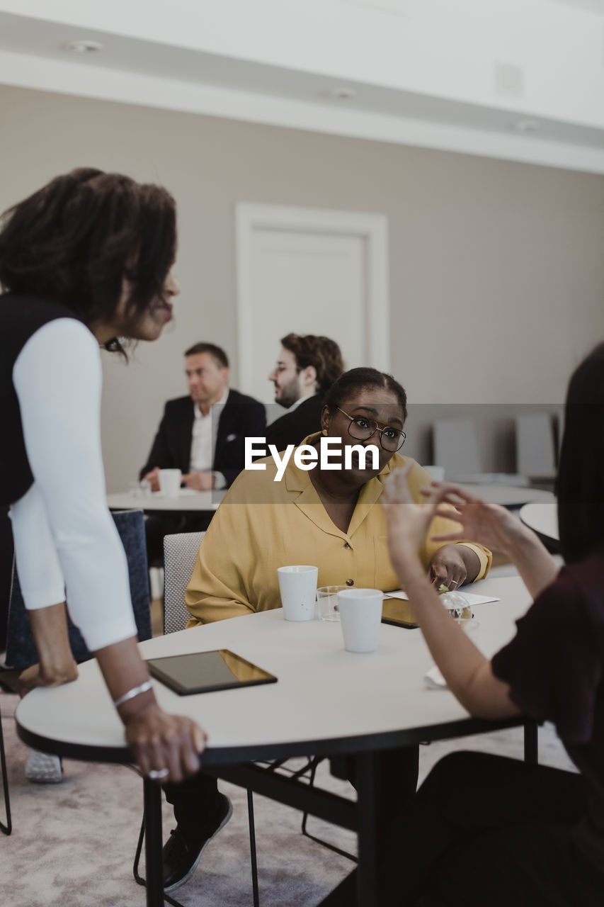 Female entrepreneurs discussing while male colleagues in background at corporate office
