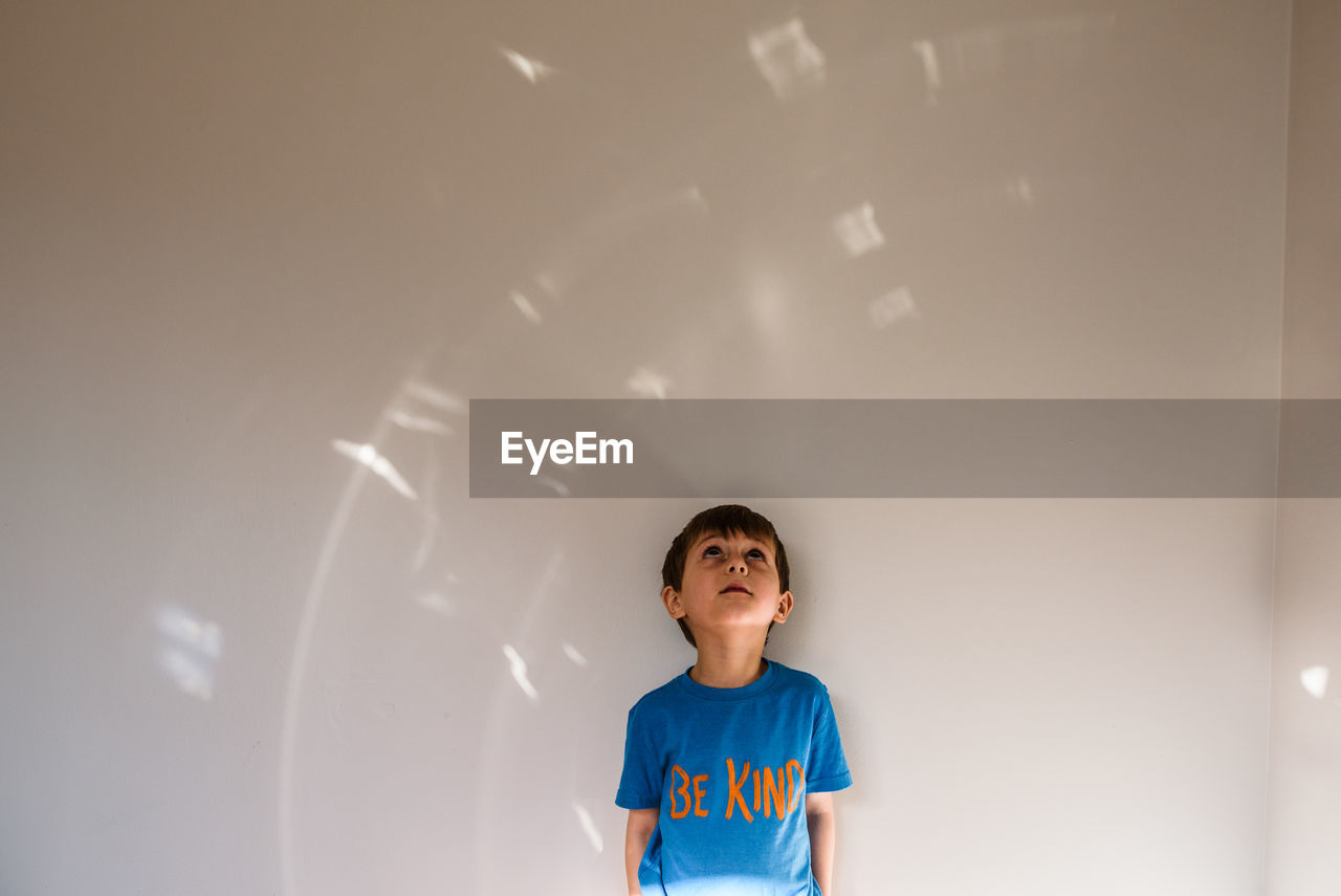 Boy wearing "be kind" shirt looking up at light pattern on wall
