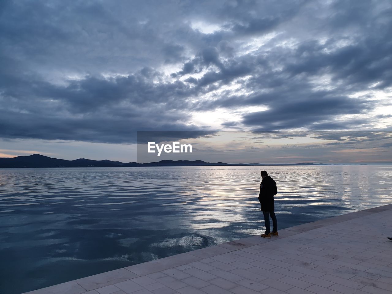 Silhouette man standing in sea against sky during sunset