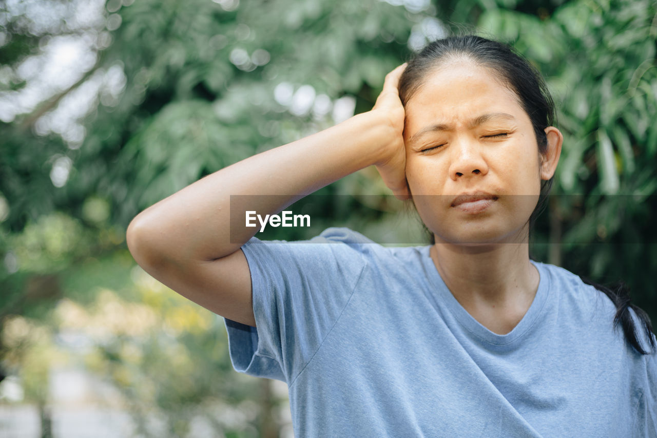 Woman touching head in pain against trees