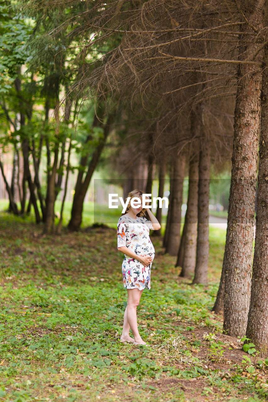 PORTRAIT OF WOMAN STANDING ON TREE TRUNK