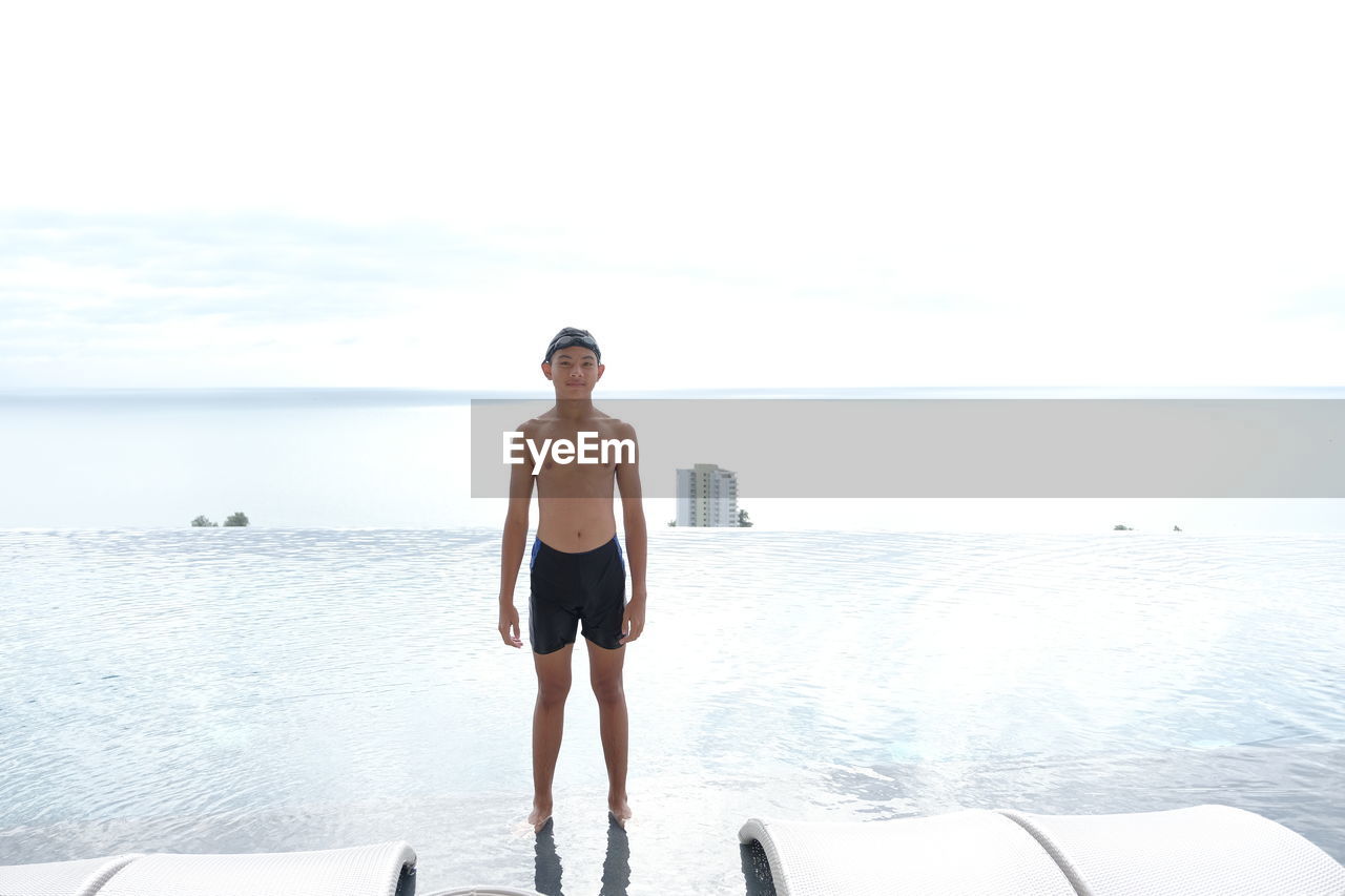 Boy standing at swimming pool with sea view