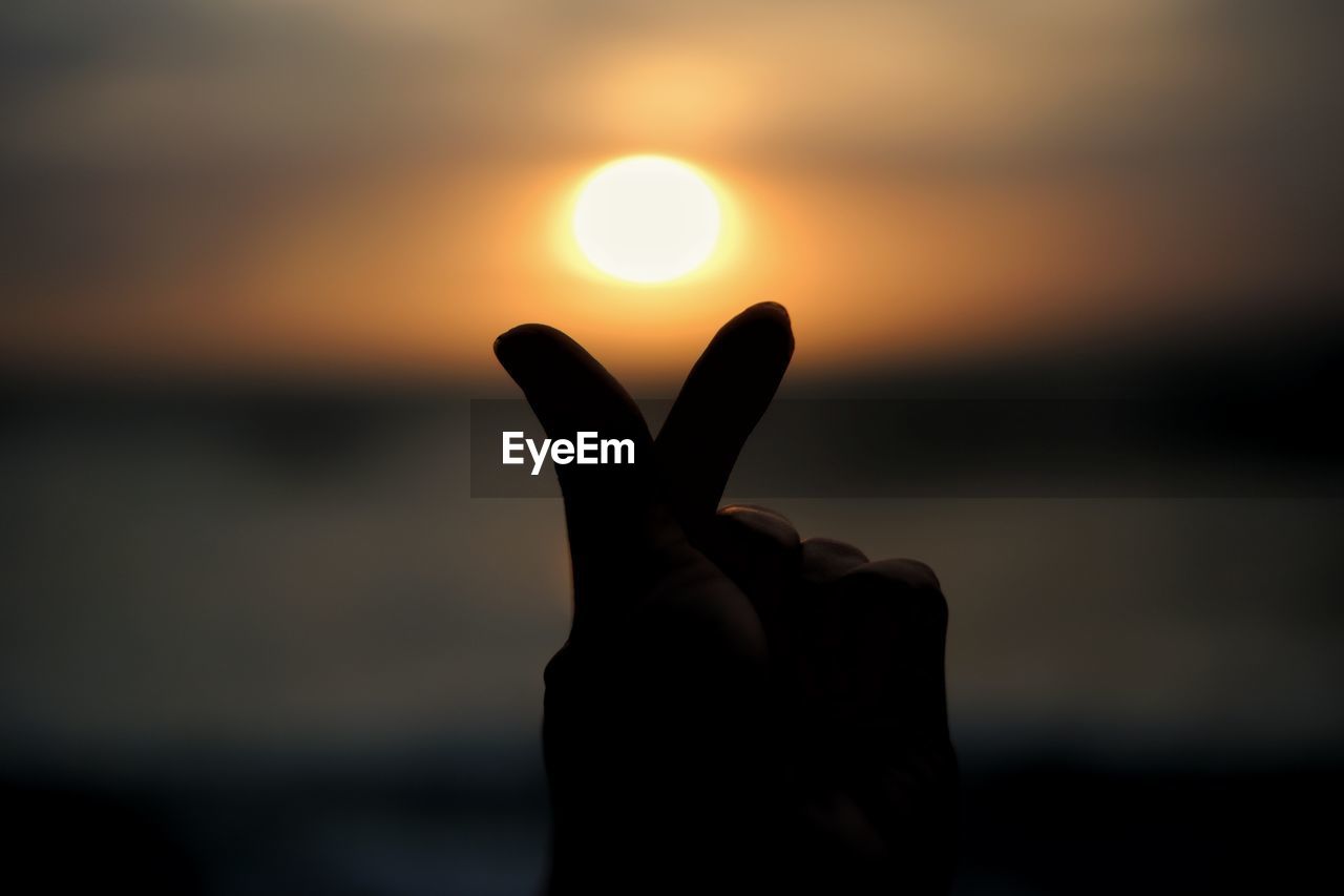 Silhouette of hand gesturing against sky during sunset