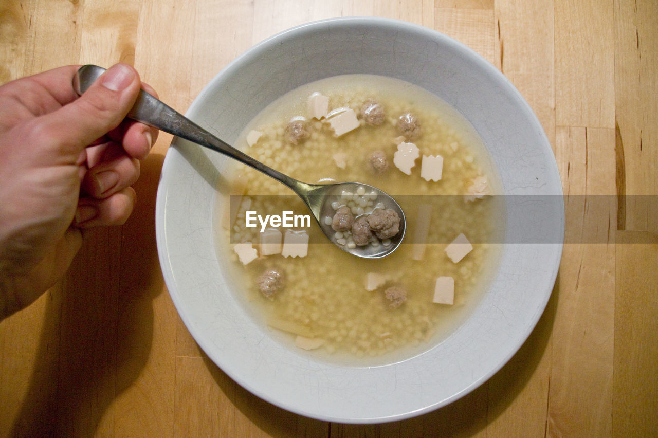Cropped hand of man holding spoon over soup bowl on table