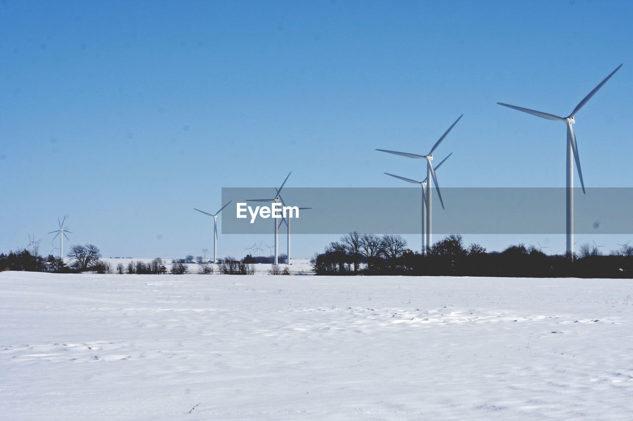 Wind turbines on snow covered field against sky