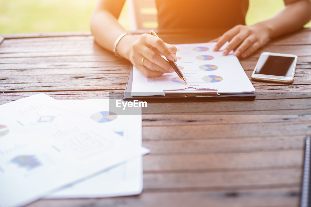 Cropped hands of woman analyzing graphs by mobile phone on table