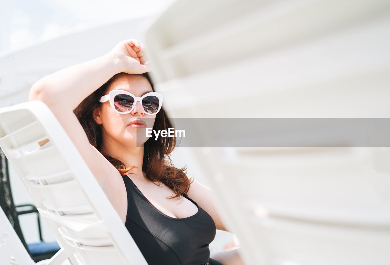 Stylish woman plus size body positive in black swimsuit on beach lounger near pool, summer vacations