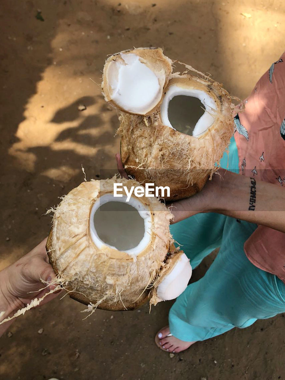 Two people holding open fresh coconuts in theo hands in a sand floor