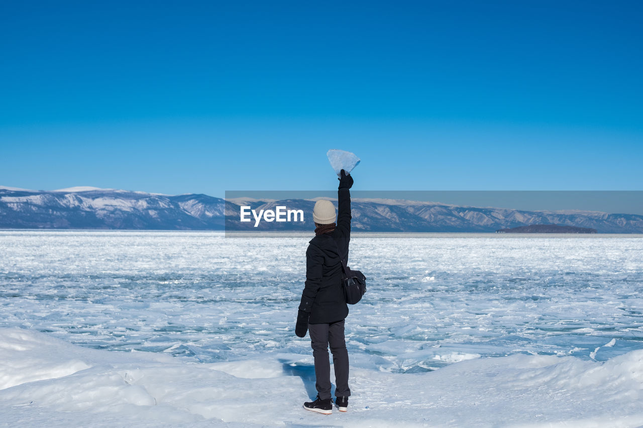 Woman standing on snowcapped mountain against blue sky