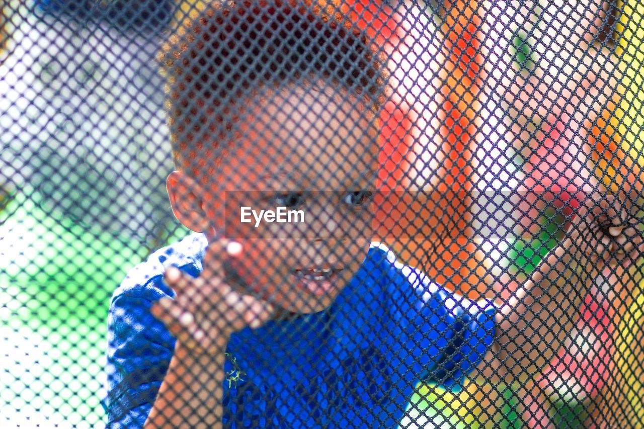 Close-up of boy looking through chainlink fence