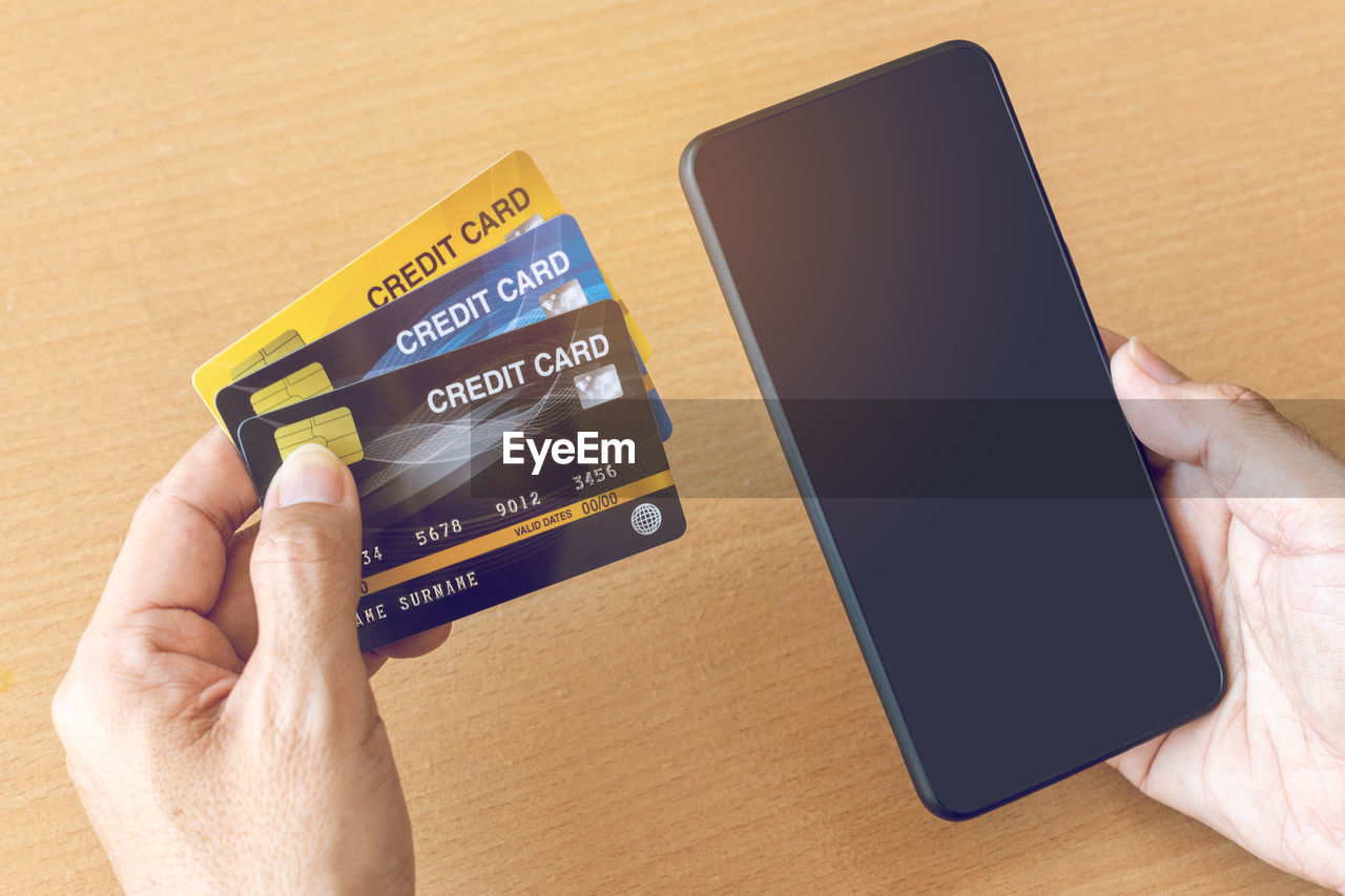 MIDSECTION OF PERSON HOLDING MOBILE PHONE ON TABLE