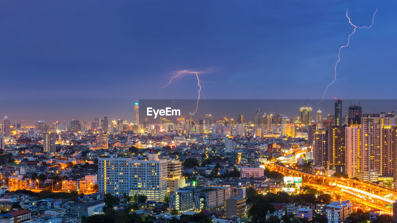 High angle view of illuminated city against lightning at dusk