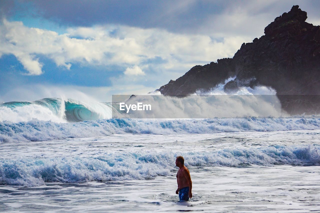 Shirtless man standing at beach against majestic waves