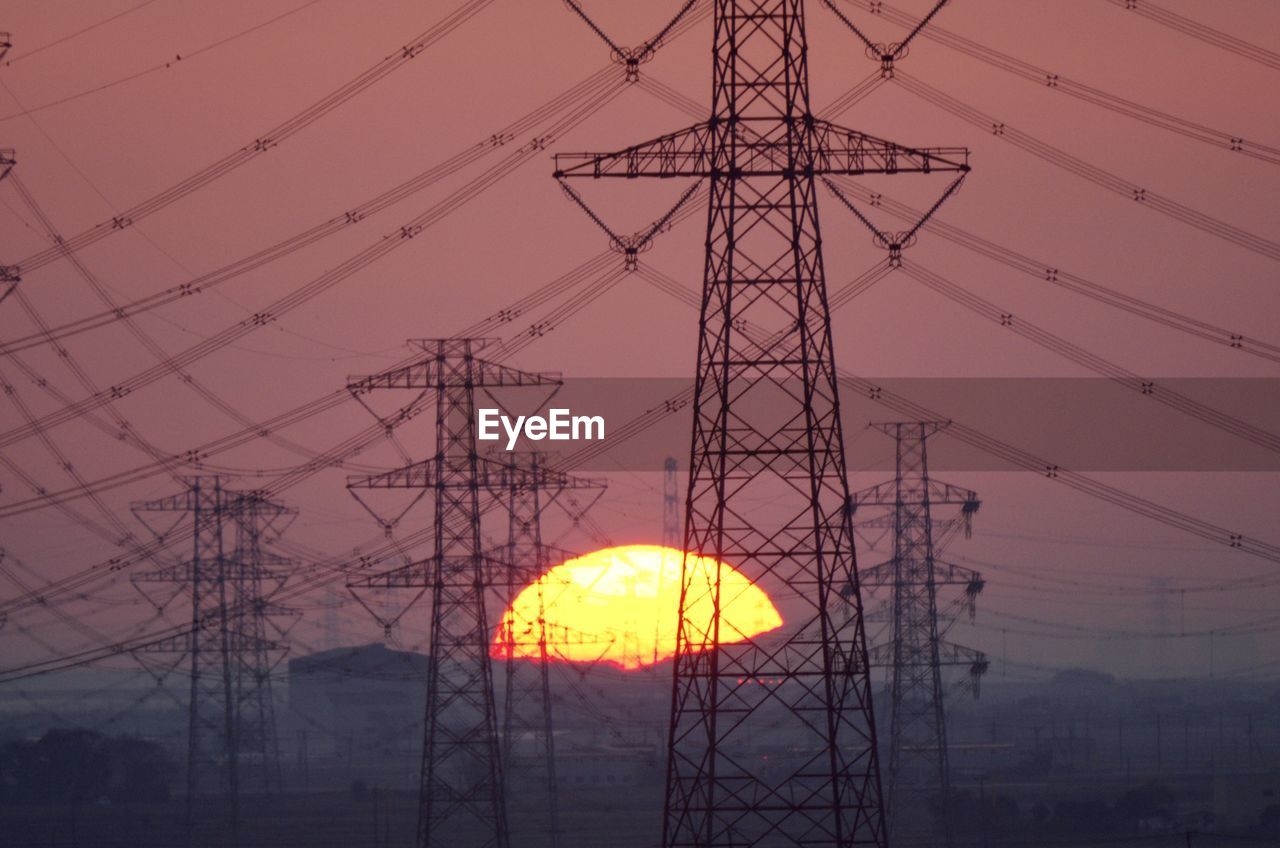 Low angle view of electricity pylon against sky during sunset