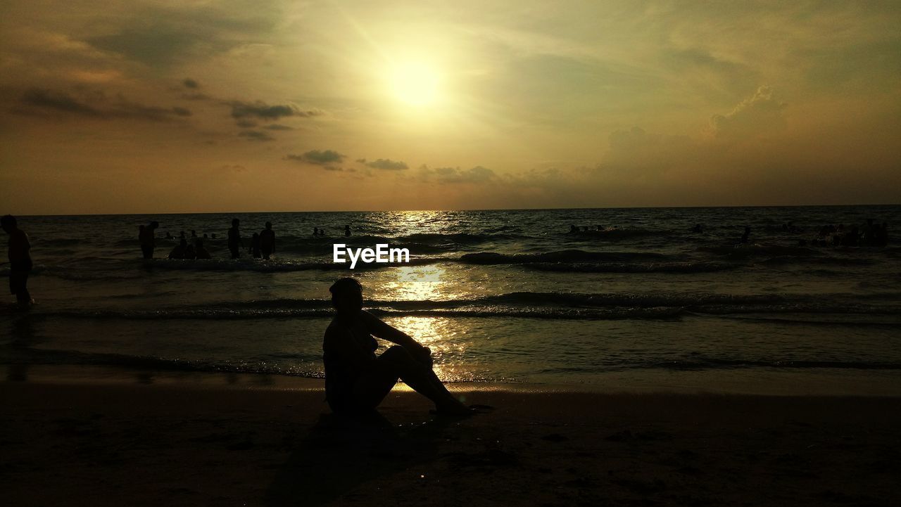 SILHOUETTE OF MAN STANDING ON BEACH AGAINST SUNSET SKY