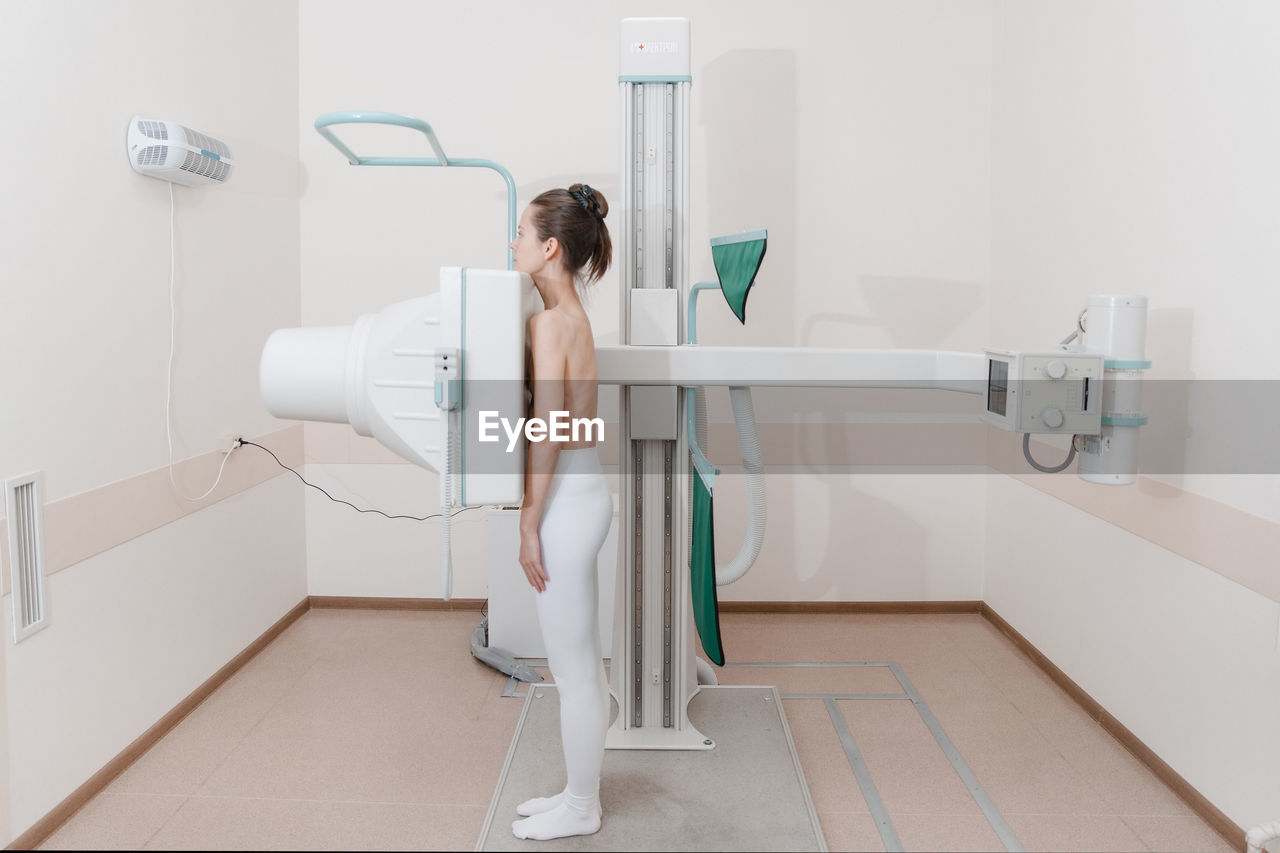 Side view of woman standing by scanning machine at clinic