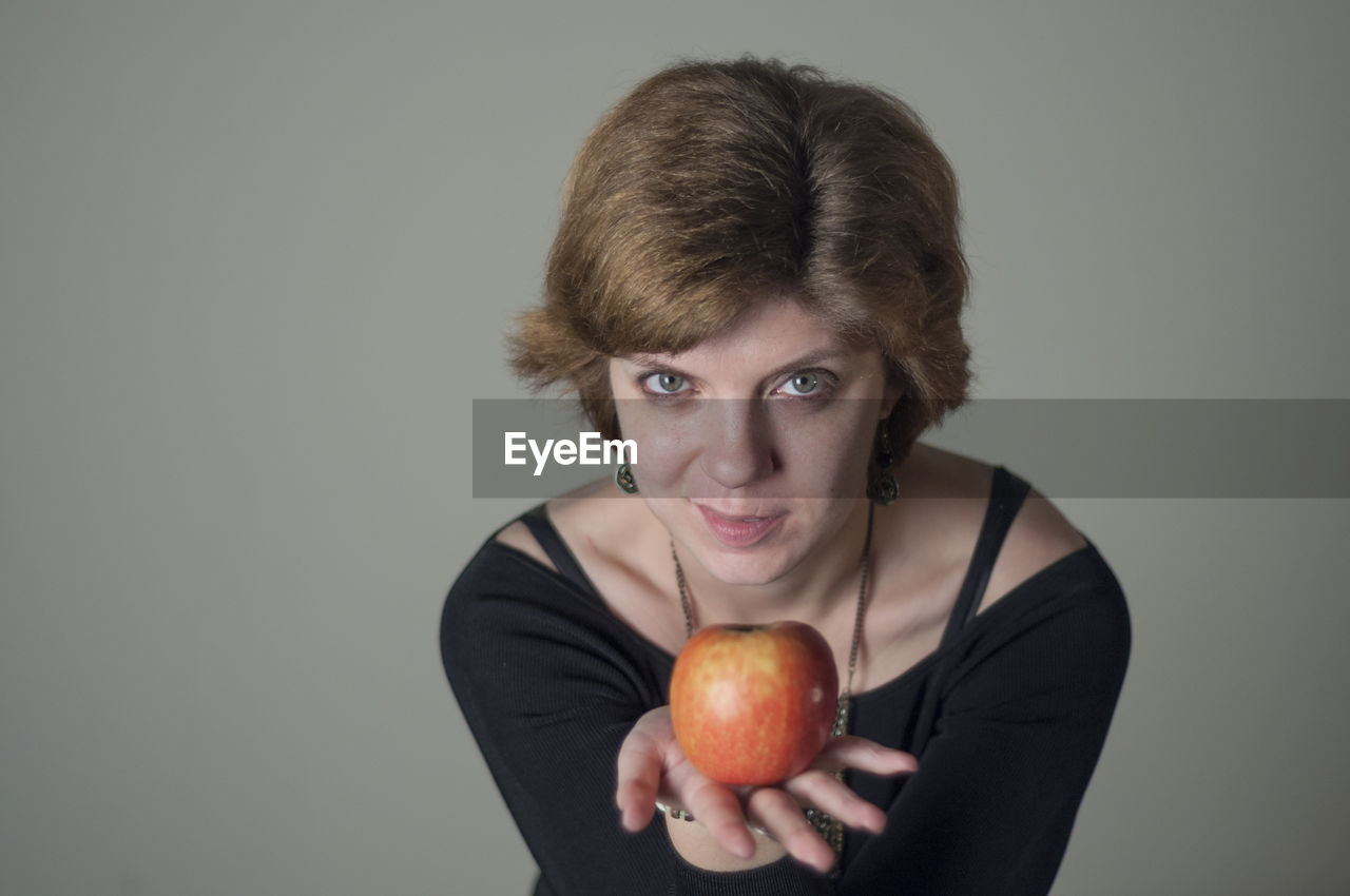 Portrait of woman holding apple against gray background