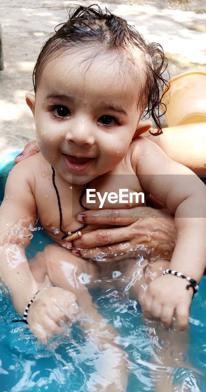 Cropped hands of woman holding naked baby in bathtub