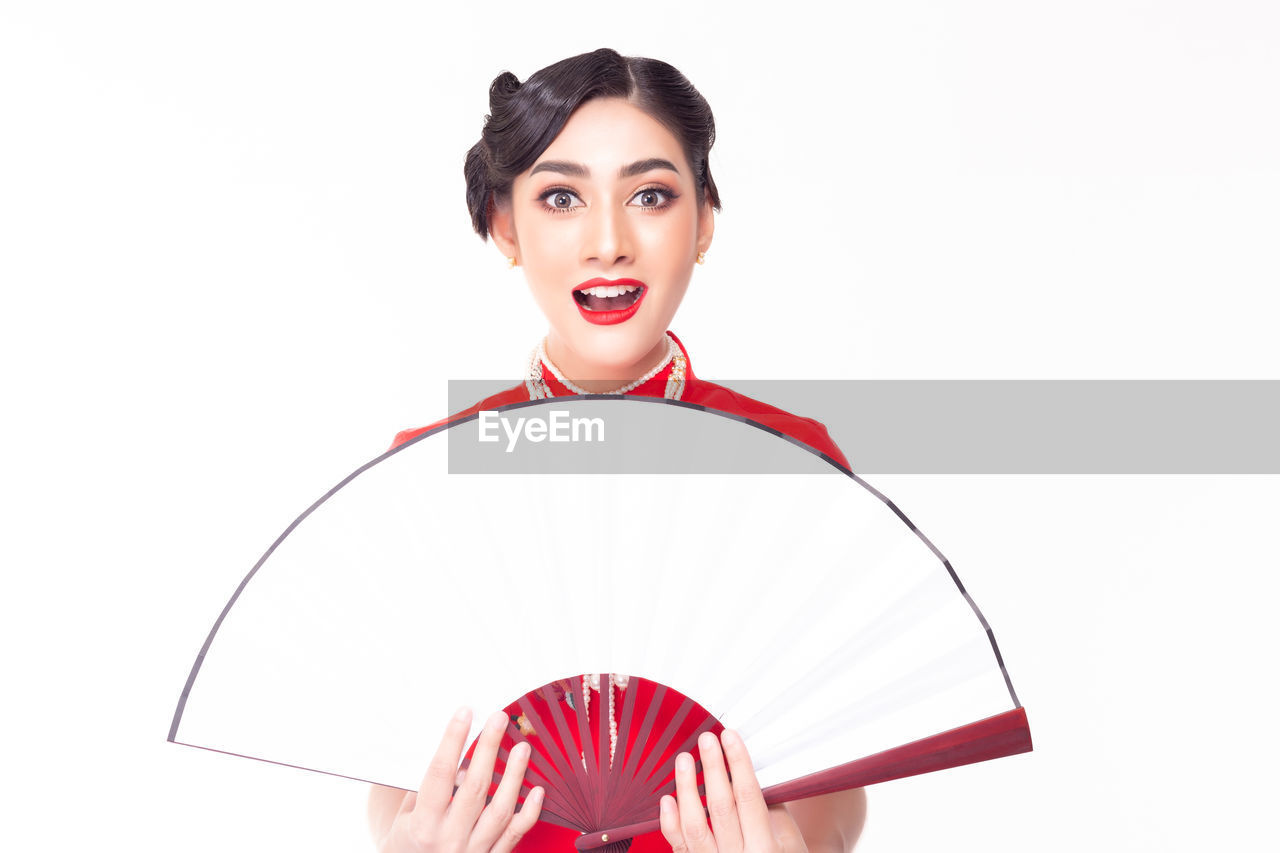 Portrait of shocked woman in red traditional clothing with hand fan against white background
