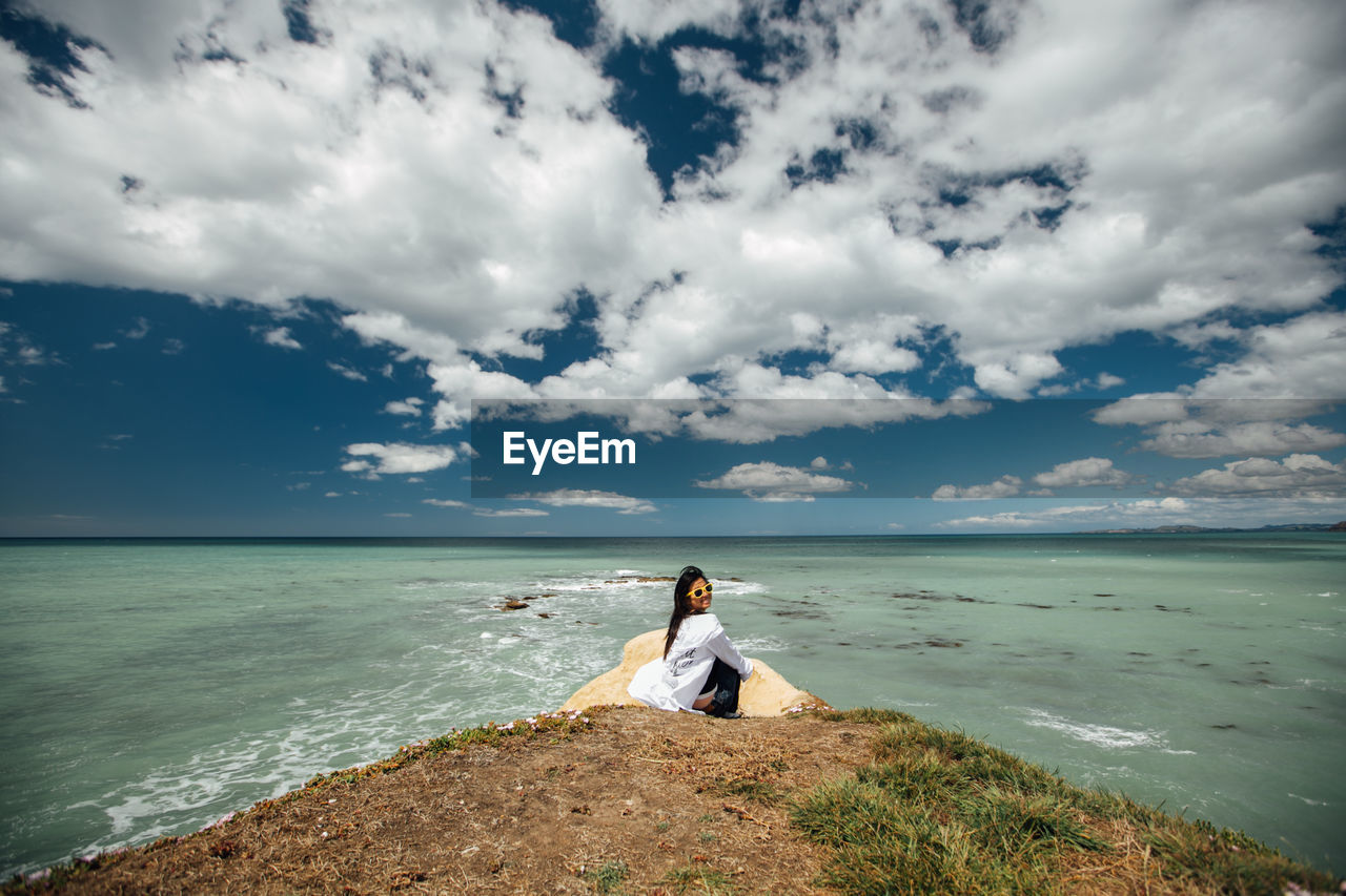 Woman sitting at beach against sky